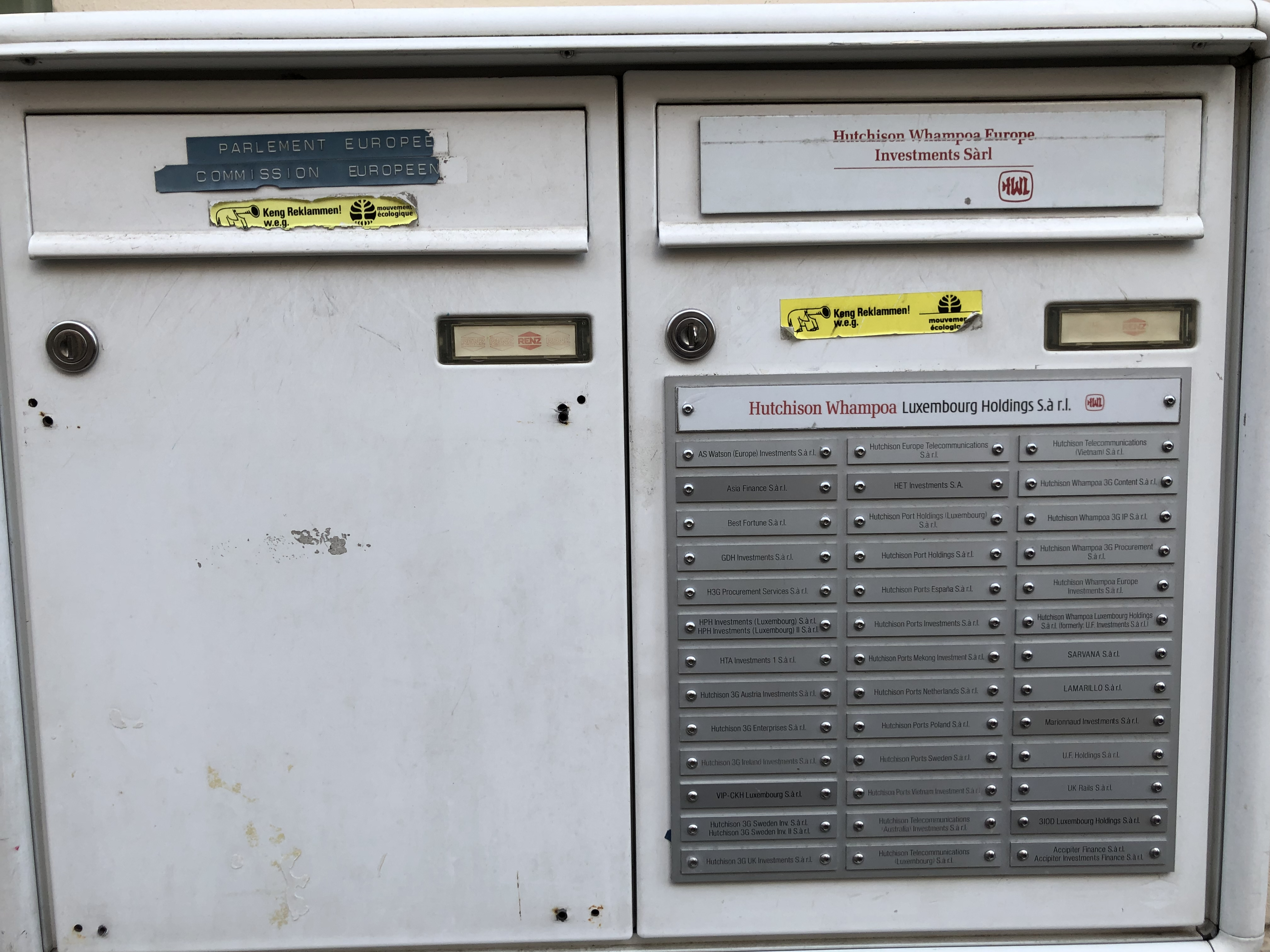 Luxembourg City, February 2018. Two mailboxes. On the left, the European Parliament and European Commission identified with strips of plastic label tape. On the right, Hutchison Whampoa Europe Investments Sàrl, with an engraved brushed-metal plaque listing forty subsidiary companies sharing the same slot.